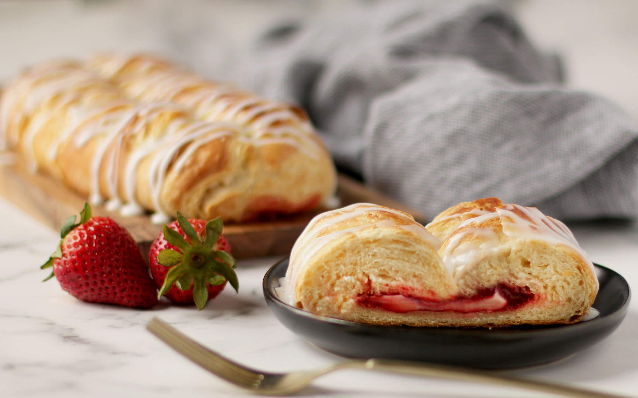 Strawberry and Cream Cheese Butter Braid Pastry with slice on plate next to fork and whole strawberries